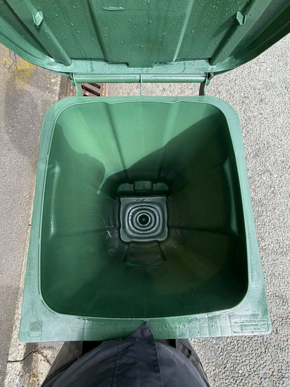 Freshly cleaned green wheelie bin with water droplets, lid open against a red brick wall