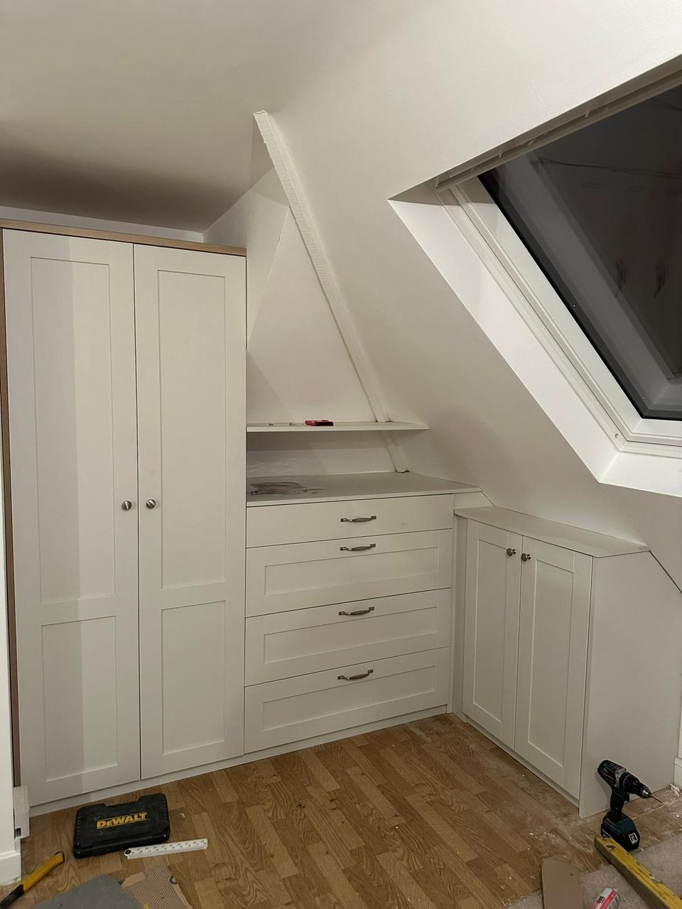 Finished loft conversion with white shaker fitted wardrobes and drawers built into the sloped eaves beneath a Velux skylight.